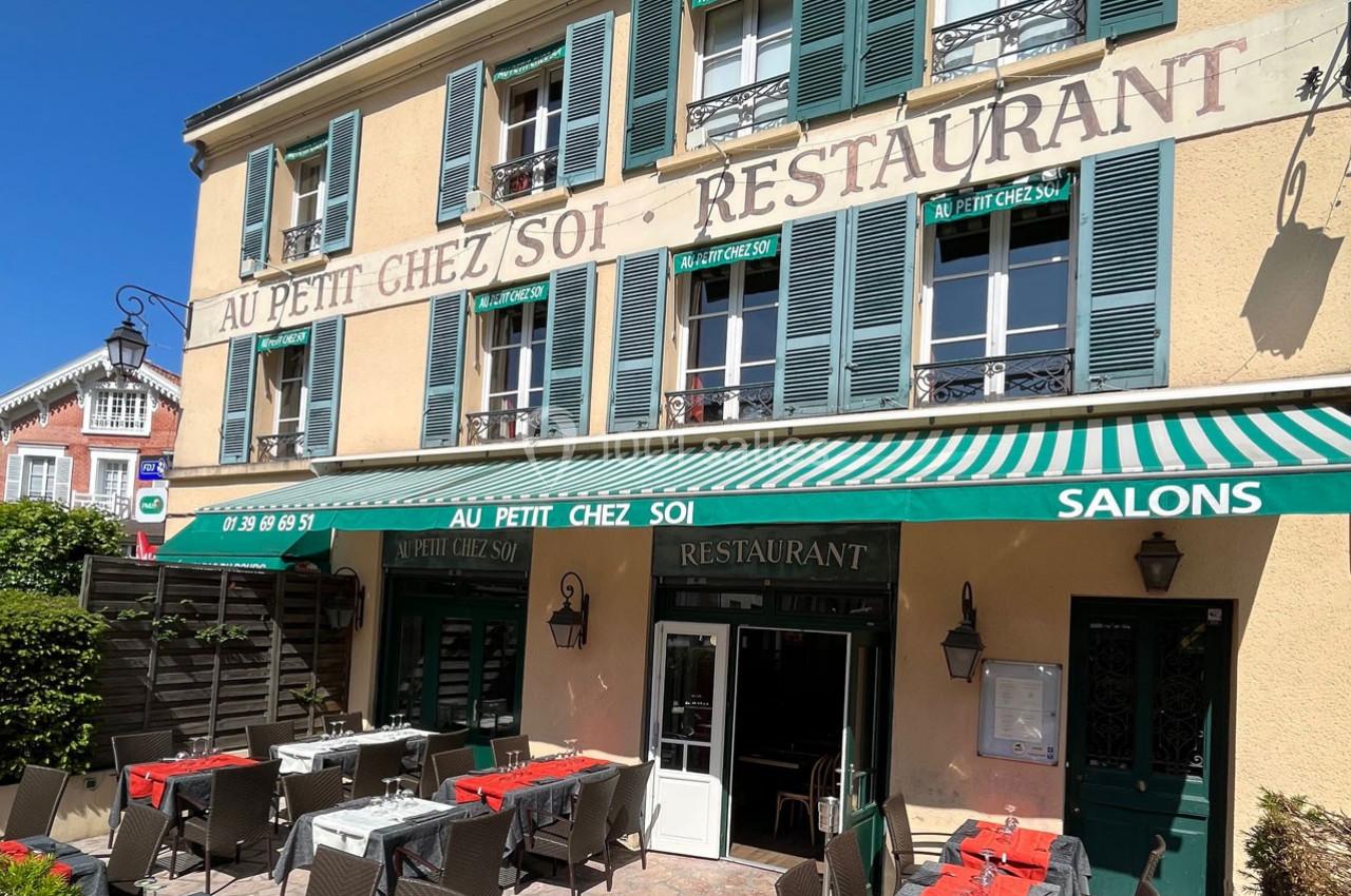 Façade d'un restaurant avec terrasse extérieure aménagée, tables dressées et store vert, par une journée ensoleillée.