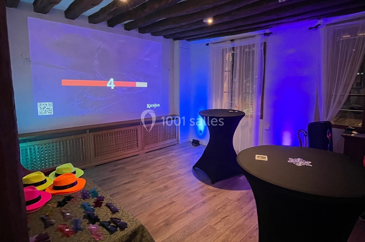 Salle éclairée avec des lumières colorées, équipée d'un écran projetant un compte à rebours et de tables décorées.