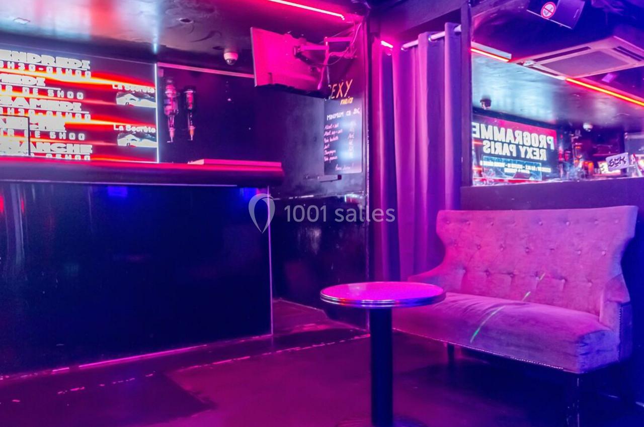 Banquette et table basse dans un espace intérieur sombre avec éclairage néon rose et décorations murales.