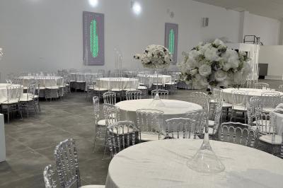 Canapé beige avec décorations dorées, tables basses et chaises blanches dans une salle ornée de panneaux lumineux bleus.