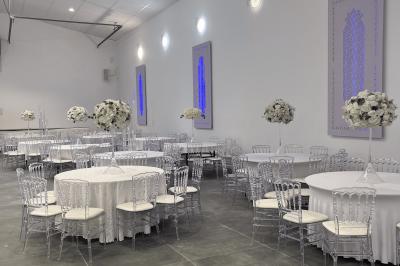 Canapé beige avec décorations dorées, tables basses et chaises blanches dans une salle ornée de panneaux lumineux bleus.
