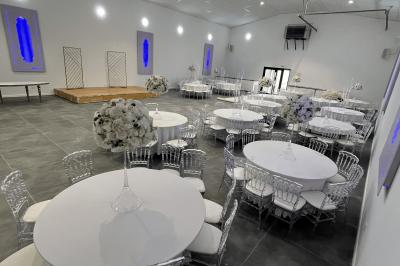 Canapé beige avec décorations dorées, tables basses et chaises blanches dans une salle ornée de panneaux lumineux bleus.
