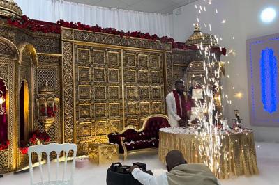 Canapé beige avec décorations dorées, tables basses et chaises blanches dans une salle ornée de panneaux lumineux bleus.