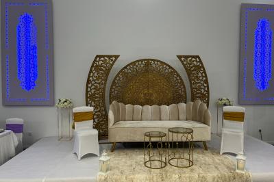 Canapé beige avec décorations dorées, tables basses et chaises blanches dans une salle ornée de panneaux lumineux bleus.