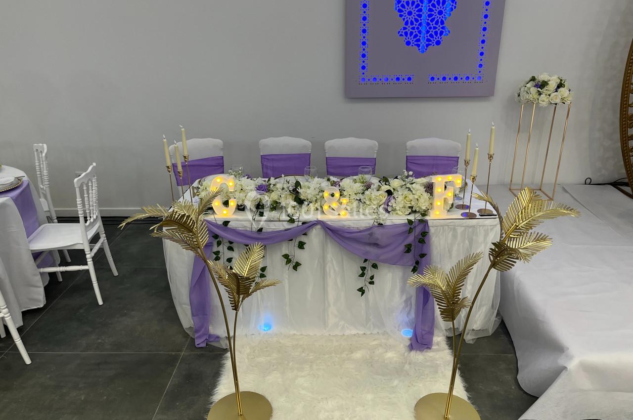 Table de mariage décorée avec des fleurs blanches, guirlandes lumineuses, nappes violettes et chandeliers dorés.
