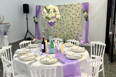 Canapé beige avec décorations dorées, tables basses et chaises blanches dans une salle ornée de panneaux lumineux bleus.