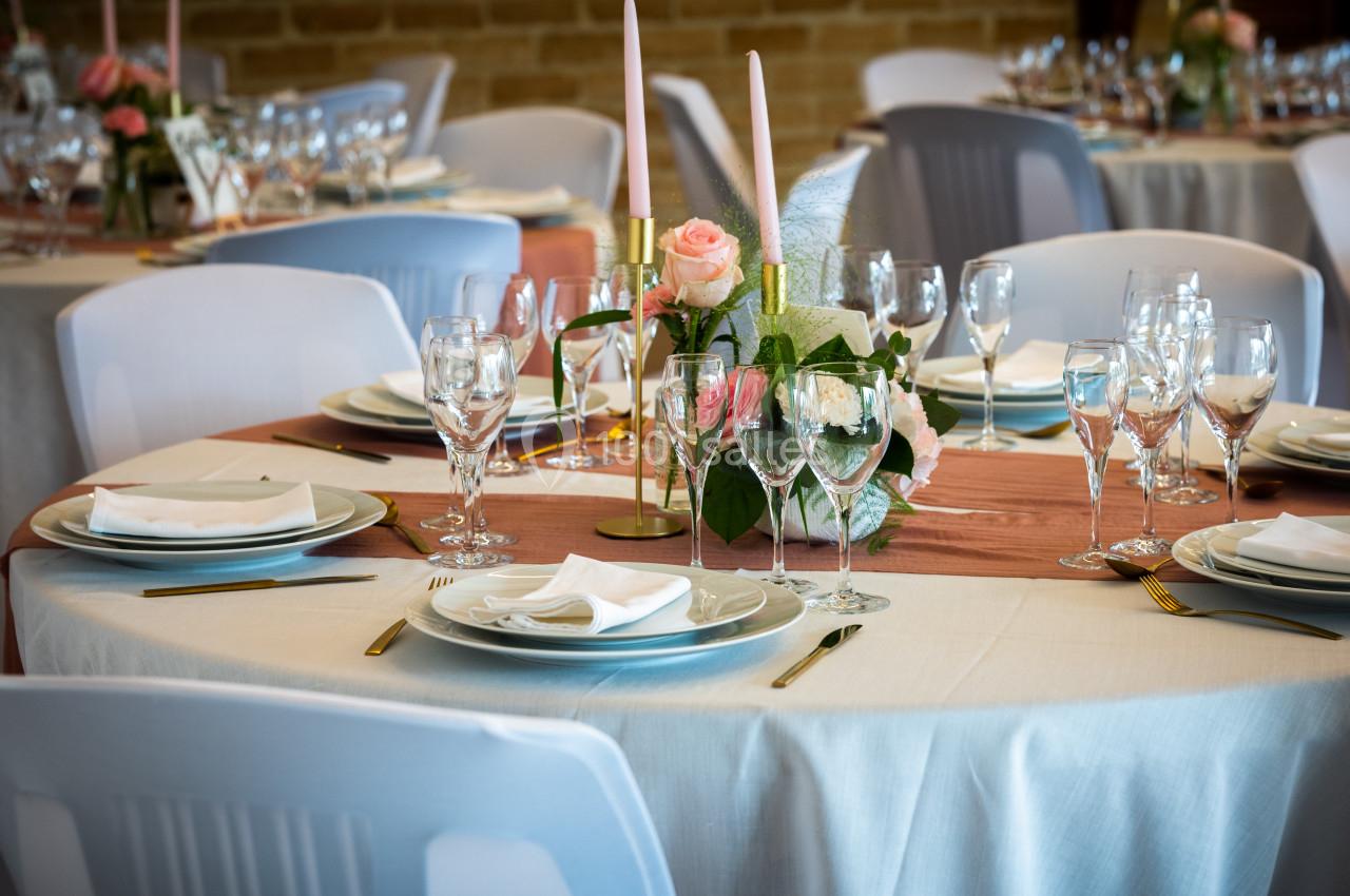 Table dressée avec nappes blanches, vaisselle élégante, bougies et centre de table floral dans une salle de réception.