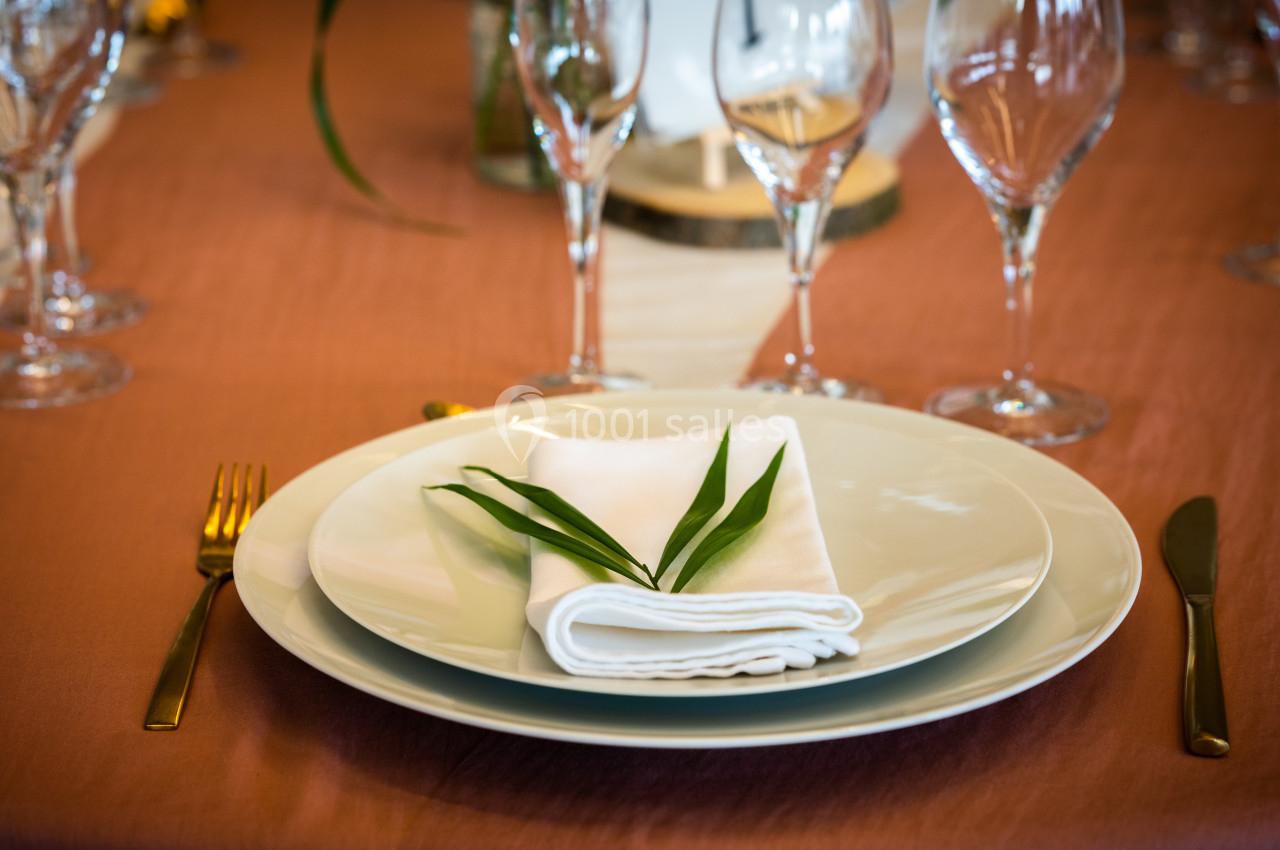 Table dressée avec une assiette blanche, une serviette pliée ornée de feuilles vertes, couverts dorés et verres à pied.
