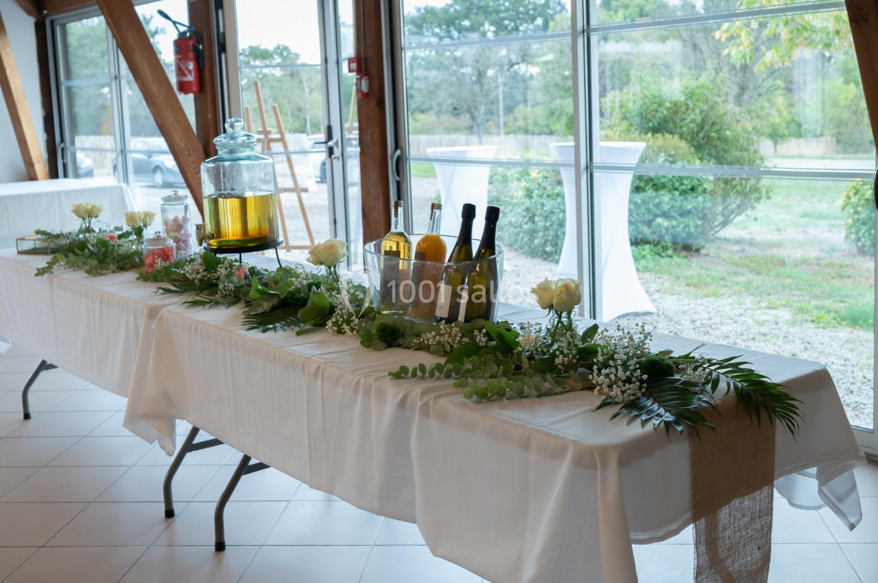 Table décorée avec nappes blanches, fleurs, feuillages, boissons et carafe, dans une salle lumineuse avec vue sur l…
