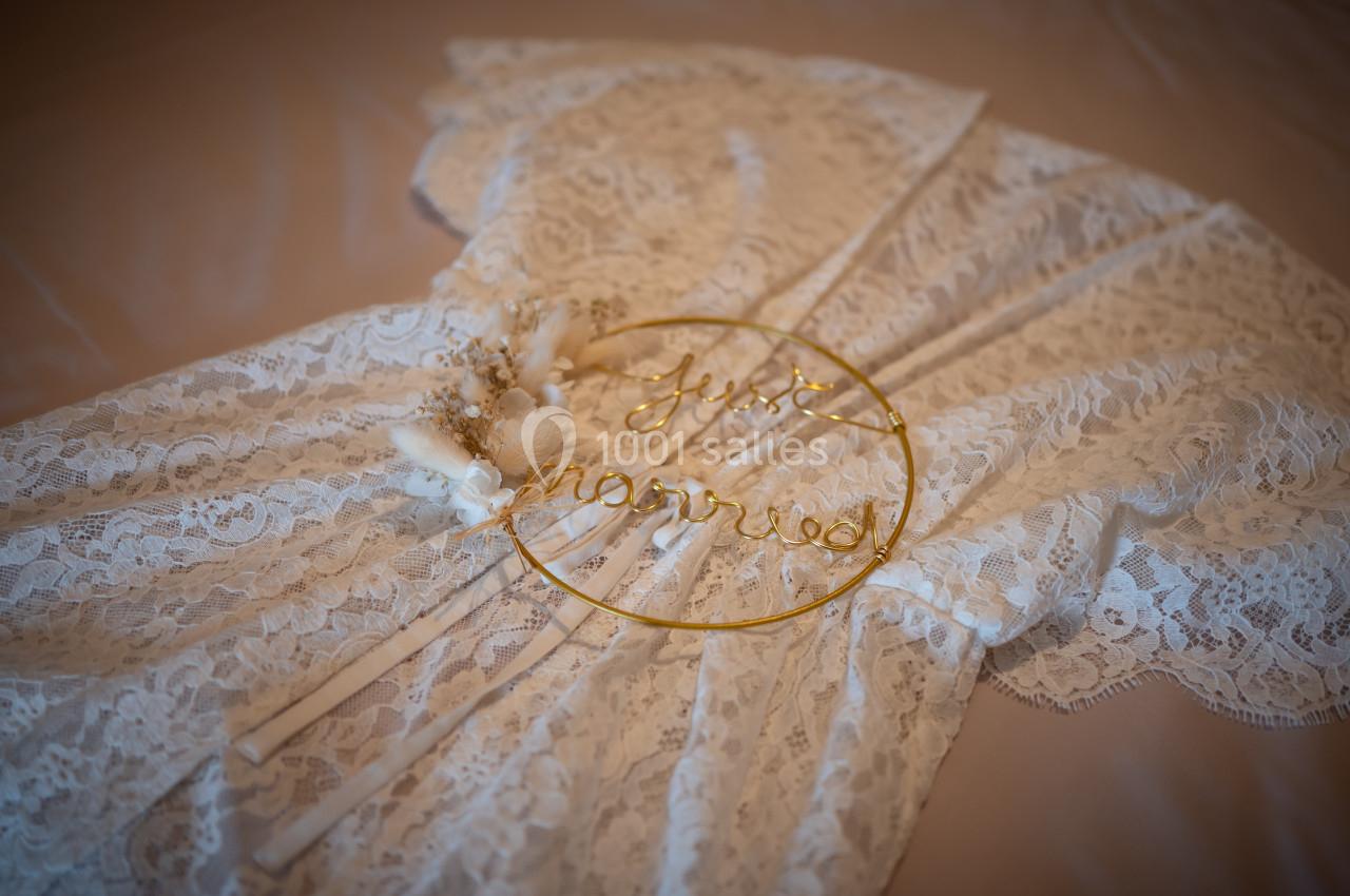 Robe en dentelle blanche posée sur un lit avec un cercle doré portant l'inscription ’just married’.