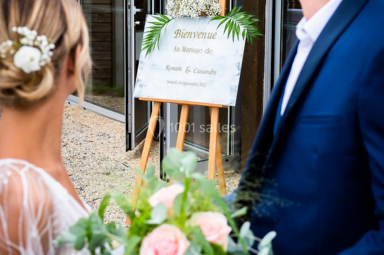 Un couple regarde un panneau de bienvenue décoré de feuillage lors d'une cérémonie de mariage en extérieur.