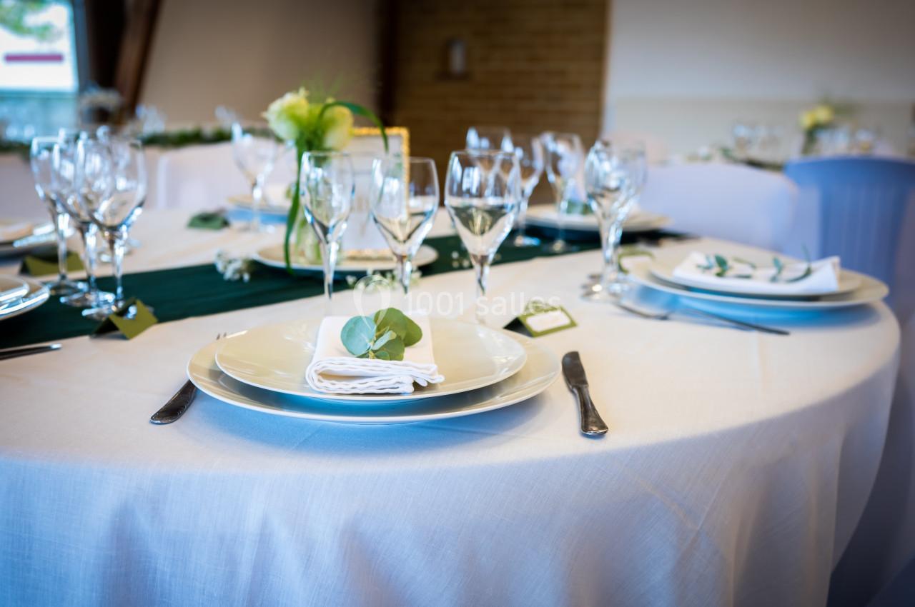 Table ronde élégamment dressée avec nappes blanches, vaisselle raffinée, verres à pied et décoration florale.