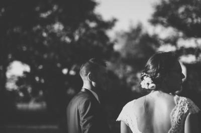 Un couple de mariés dans un jardin, la mariée tenant un bouquet de roses pastel au premier plan.