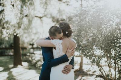 Un couple de mariés dans un jardin, la mariée tenant un bouquet de roses pastel au premier plan.