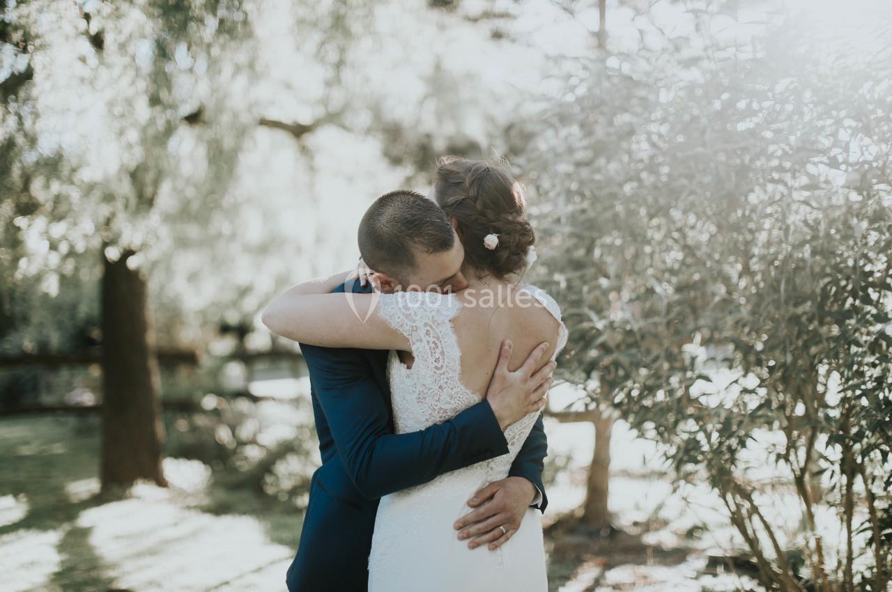 Un couple s'enlace tendrement dans un jardin ensoleillé, entouré de verdure.