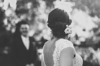 Un couple de mariés dans un jardin, la mariée tenant un bouquet de roses pastel au premier plan.