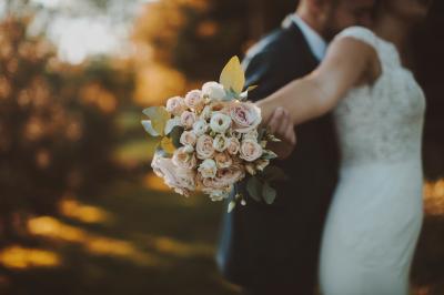 Un couple de mariés dans un jardin, la mariée tenant un bouquet de roses pastel au premier plan.