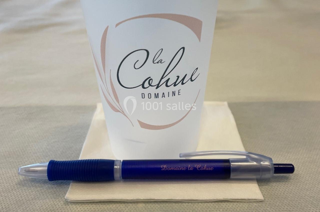 Gobelet réutilisable et stylo bleu posés sur une serviette blanche, sur une table beige.