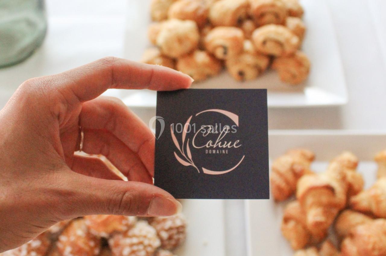 Une main tenant une carte devant des assiettes de viennoiseries variées sur une nappe blanche.