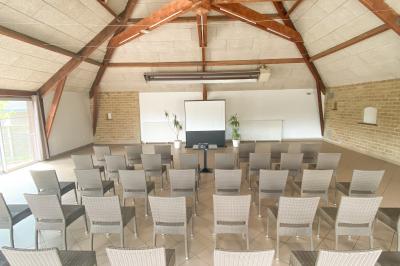 Salle de réunion lumineuse avec des chaises disposées en rangées face à un écran de projection et un tableau blanc.