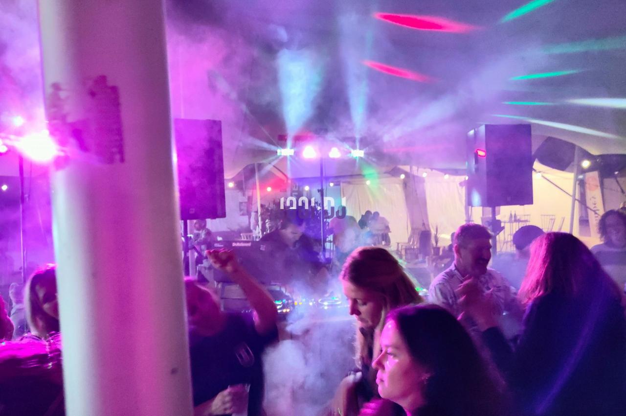 Personnes dansant sous des jeux de lumière colorés et de la fumée dans une ambiance festive en intérieur.