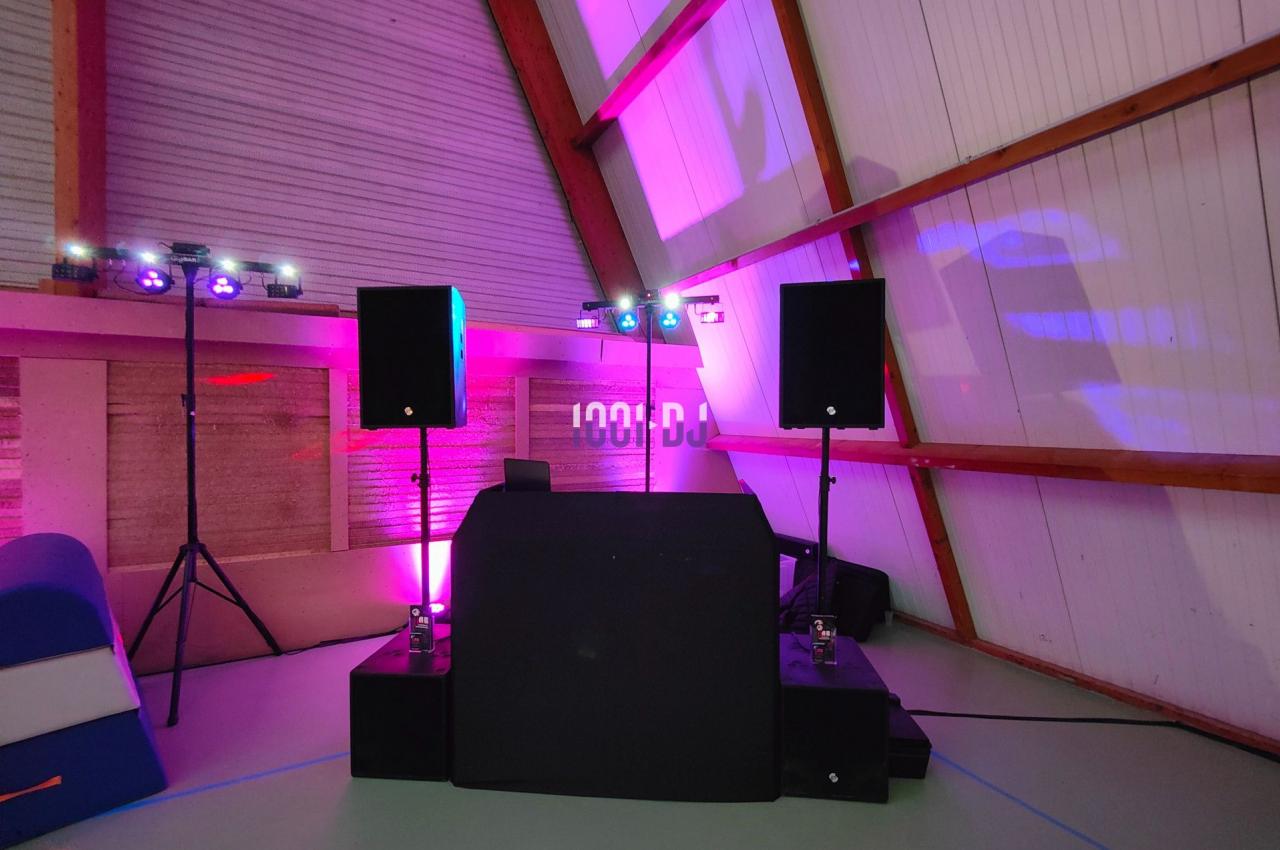 Console de DJ avec enceintes et éclairages colorés dans une salle aux murs en bois et plafond incliné.