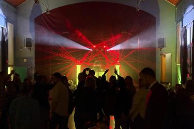 Salle de spectacle avec un public debout et assis, décorations festives et scène éclairée avec une présentation en cours.