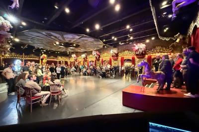 Salle de spectacle avec un public debout et assis, décorations festives et scène éclairée avec une présentation en cours.