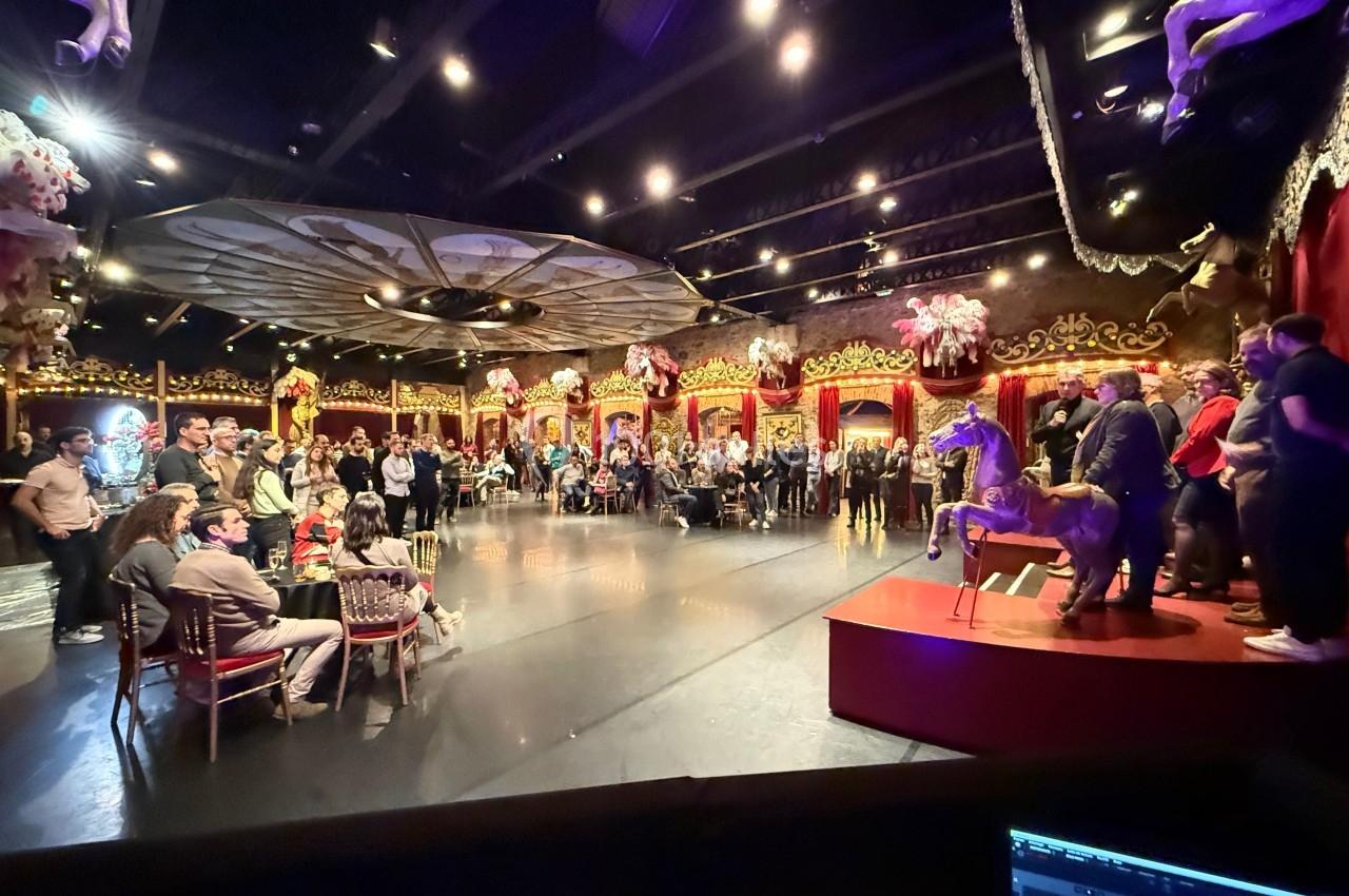 Salle de spectacle avec un public debout et assis, décorations festives et scène éclairée avec une présentation en cours.