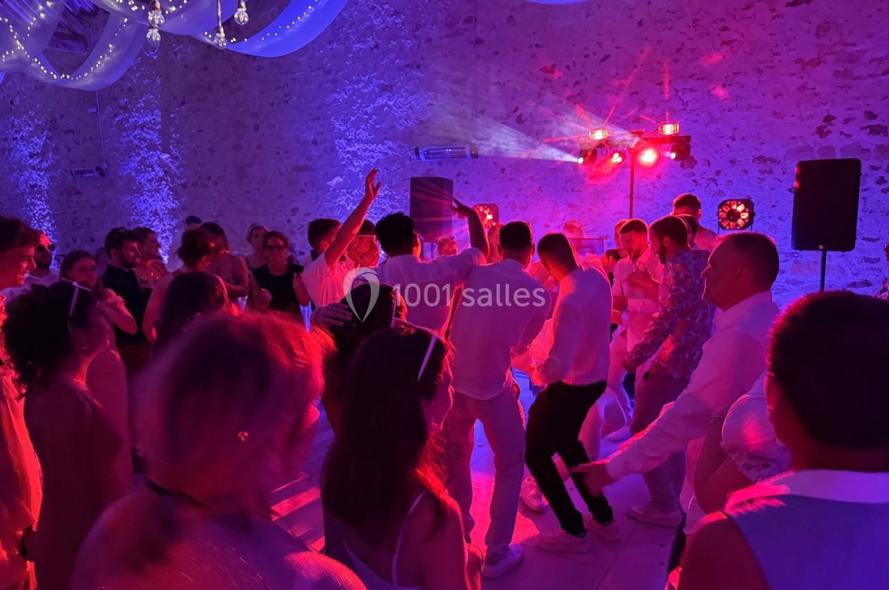 Groupe de personnes dansant sous des lumières colorées dans une salle en pierre décorée de voilages suspendus.