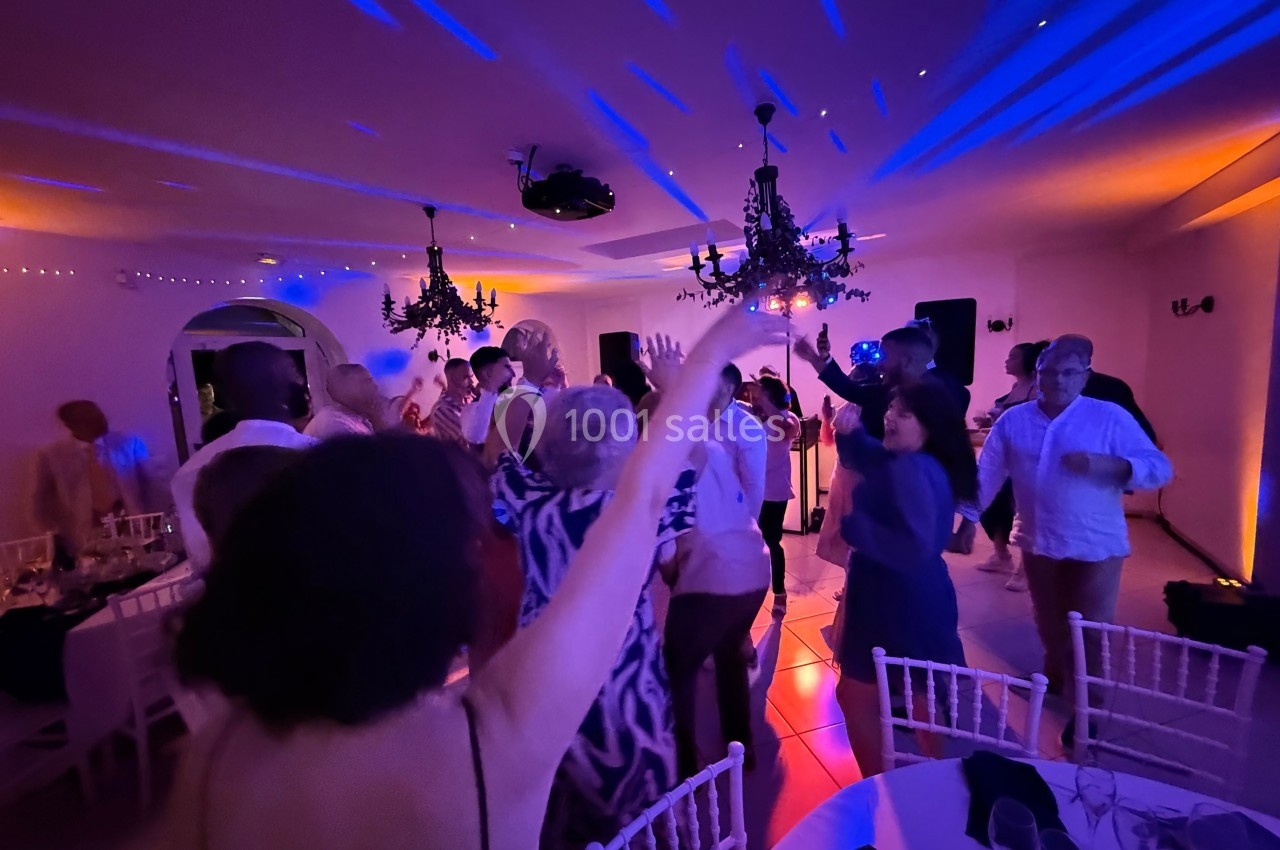 Des personnes dansent sous des lumières colorées dans une salle décorée avec des chandeliers suspendus.