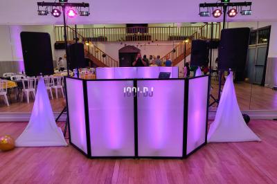 Poste de DJ éclairé en violet avec des haut-parleurs et des lumières dans une salle au décor classique.