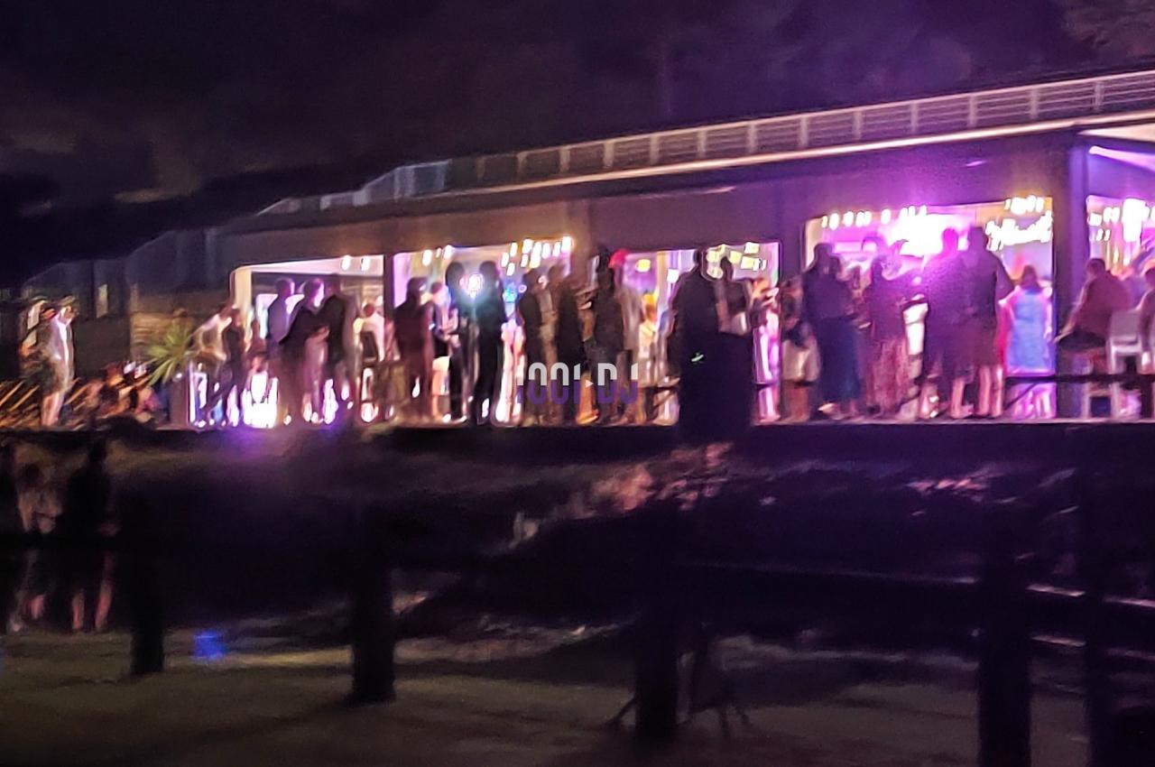 Groupe de personnes rassemblées devant un bâtiment illuminé, de nuit, avec une ambiance festive.