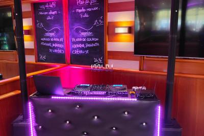 Poste de DJ éclairé en violet avec des haut-parleurs et des lumières dans une salle au décor classique.