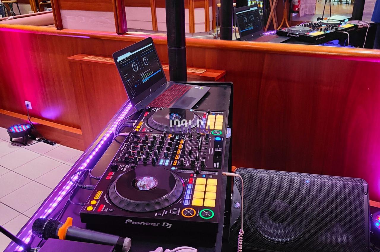 Poste de DJ avec platines, casque audio et ordinateur dans un espace intérieur avec tables et éclairage tamisé.