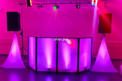 Poste de DJ éclairé en violet avec des haut-parleurs et des lumières dans une salle au décor classique.