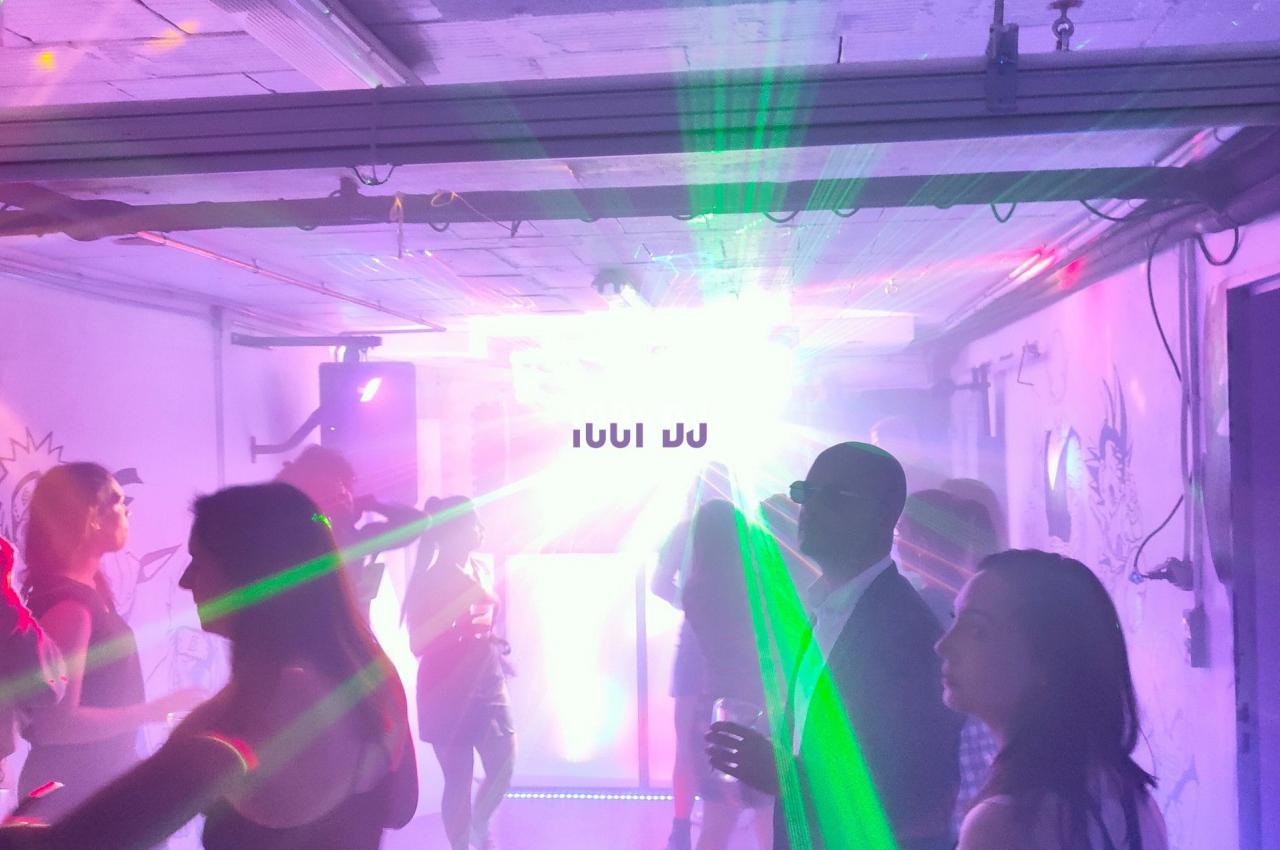 Des personnes dansent dans une pièce éclairée par des lumières colorées et un effet lumineux intense au centre.