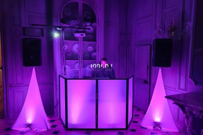 Poste de DJ éclairé en violet avec des haut-parleurs et des lumières dans une salle au décor classique.