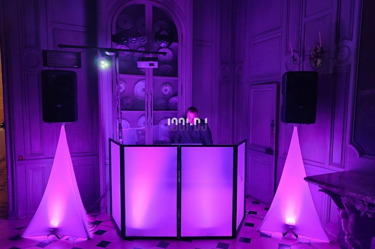 Poste de DJ éclairé en violet avec des haut-parleurs et des lumières dans une salle au décor classique.