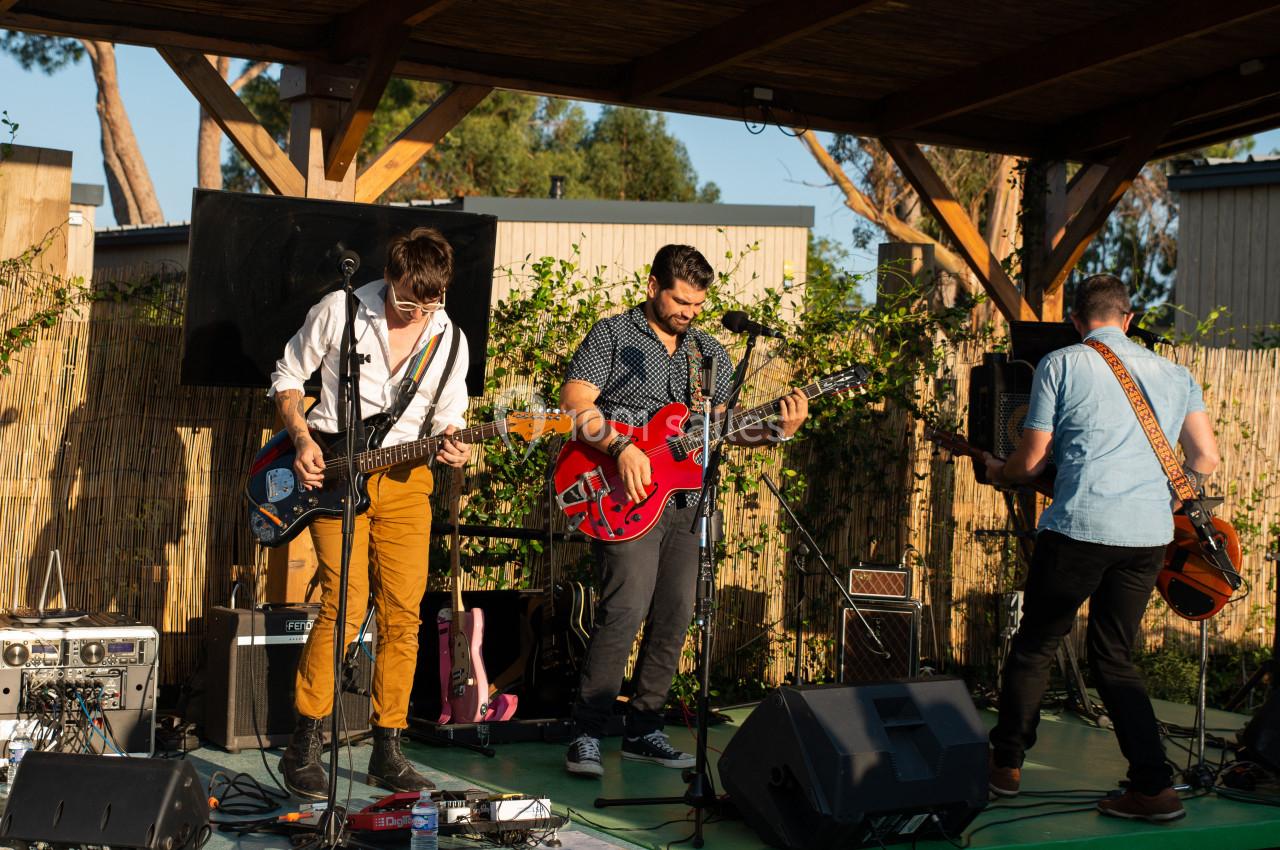 Un groupe de musiciens joue en plein air sous une structure en bois, entouré de végétation.