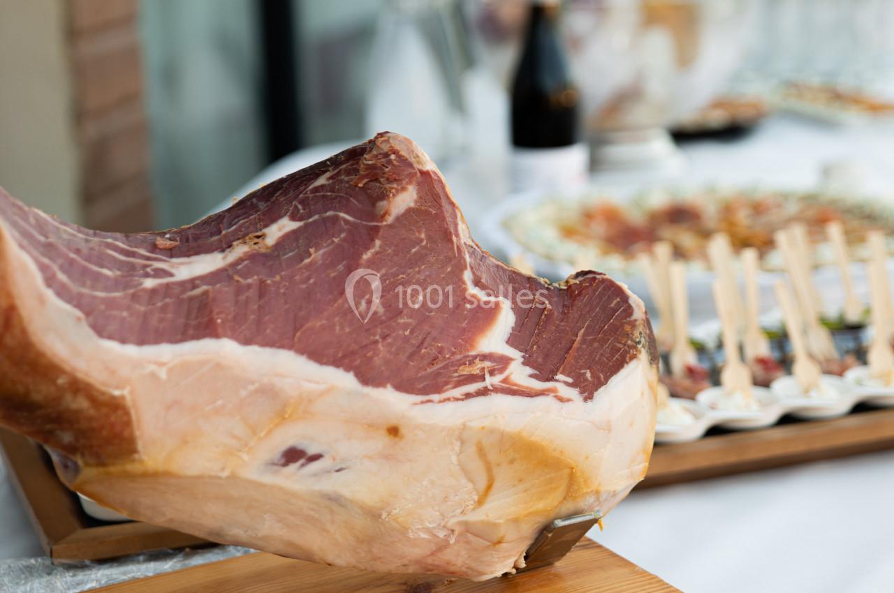 Jambon cru sur un support en bois, avec un buffet flou en arrière-plan.