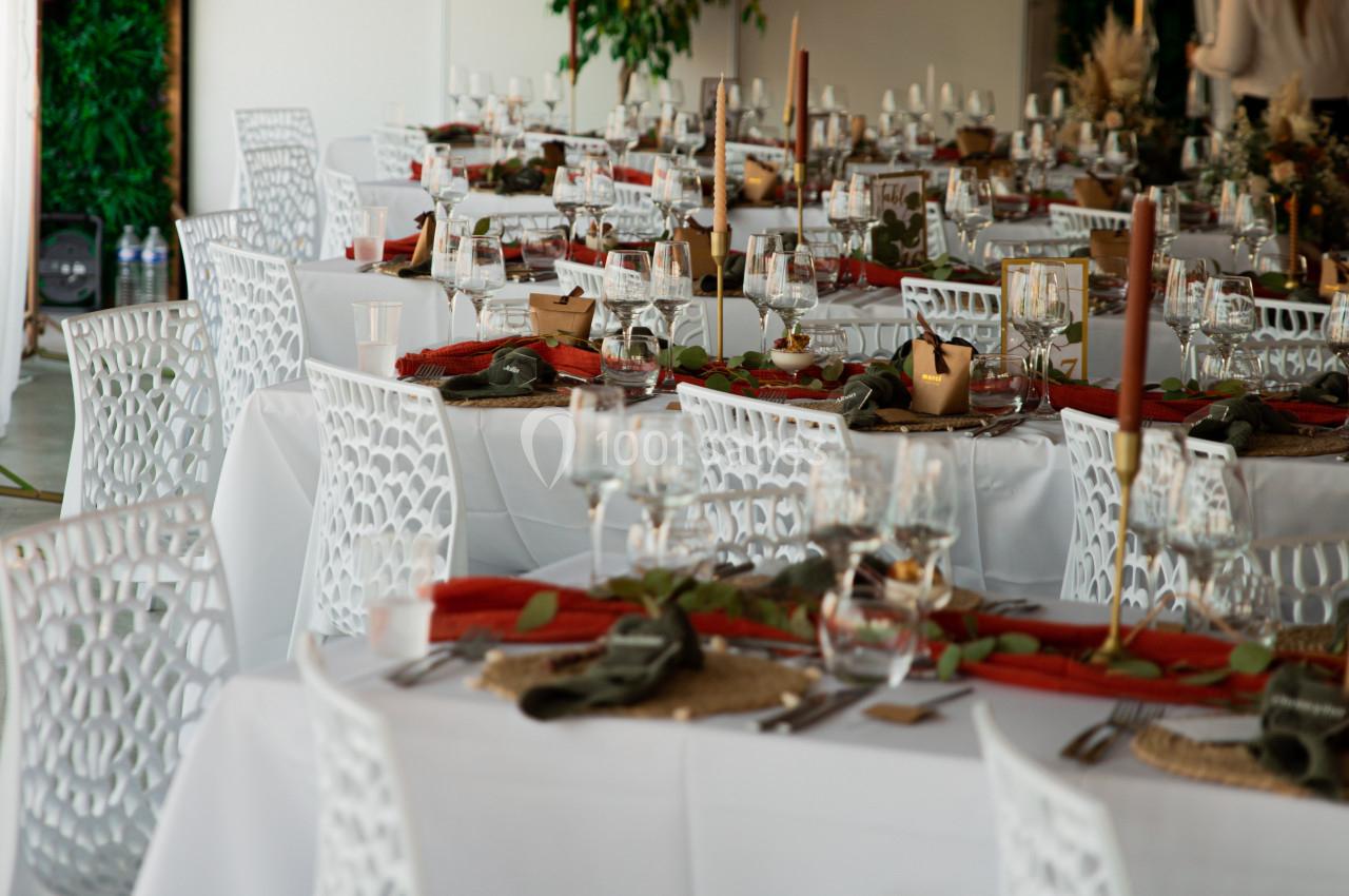 Salle décorée pour un événement avec des tables dressées, nappes blanches, bougies et éléments végétaux.