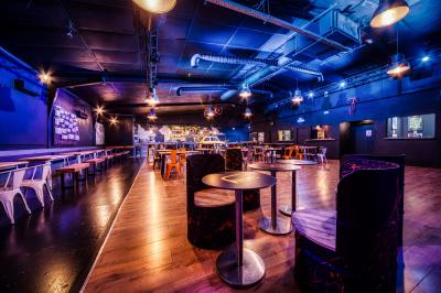Terrasse extérieure avec tables, chaises et parasols orange, entourée de végétation, devant un bâtiment en bois et métal.