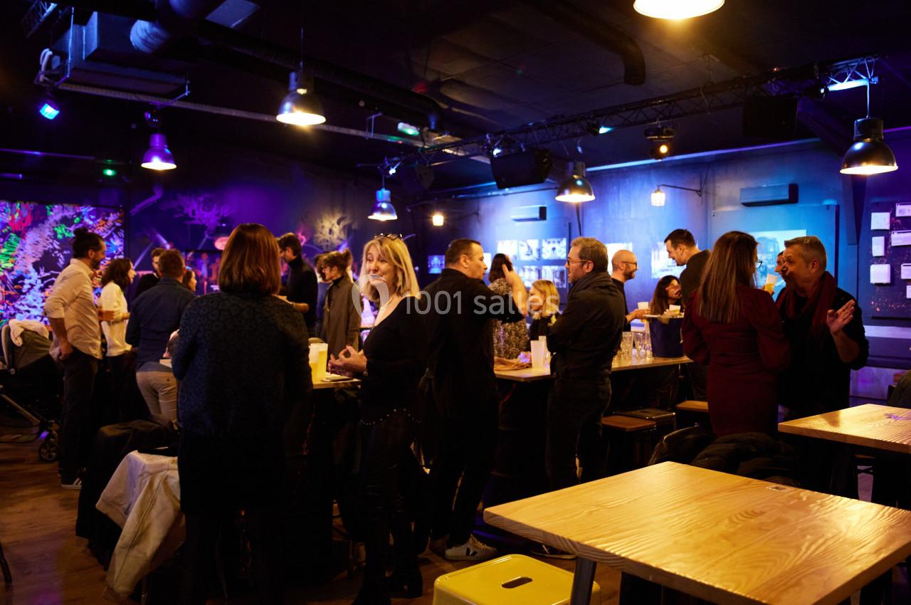 Groupe de personnes discutant dans un espace intérieur animé, éclairé par des lumières colorées.