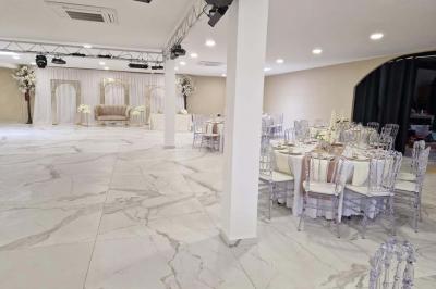 Salle de réception décorée avec des fleurs blanches, un canapé élégant sur une estrade et des tables dressées.