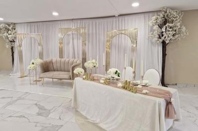 Salle de réception décorée avec des fleurs blanches, un canapé élégant sur une estrade et des tables dressées.