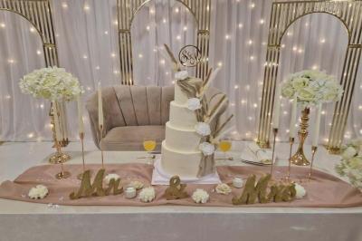 Salle de réception décorée avec des fleurs blanches, un canapé élégant sur une estrade et des tables dressées.