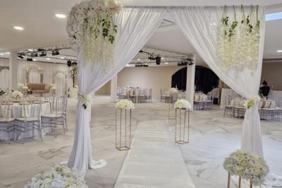 Salle de réception décorée avec des fleurs blanches, un canapé élégant sur une estrade et des tables dressées.