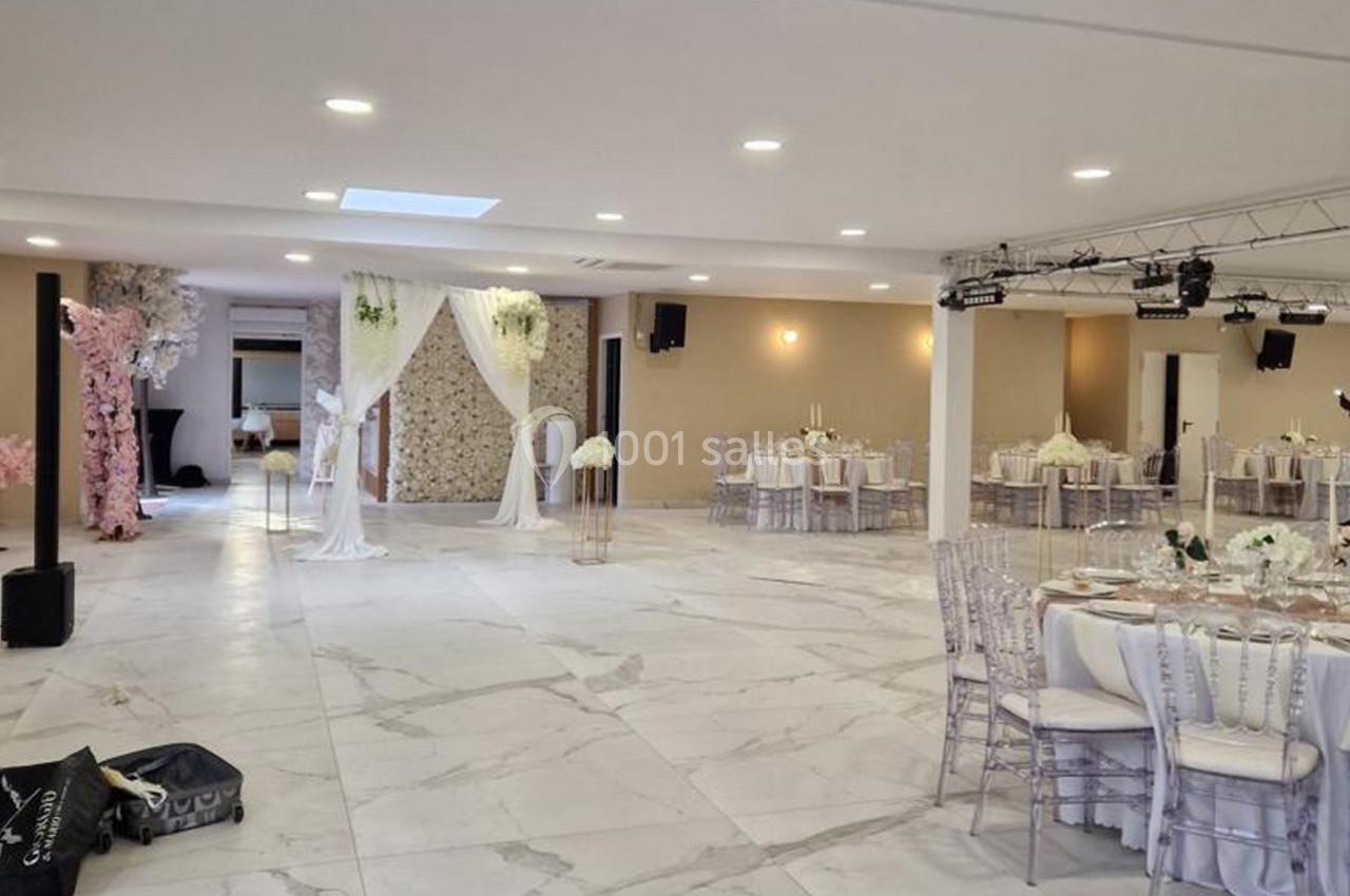 Salle de réception lumineuse avec tables dressées, chaises transparentes et décorations florales élégantes.