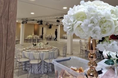 Salle de réception décorée avec des fleurs blanches, un canapé élégant sur une estrade et des tables dressées.